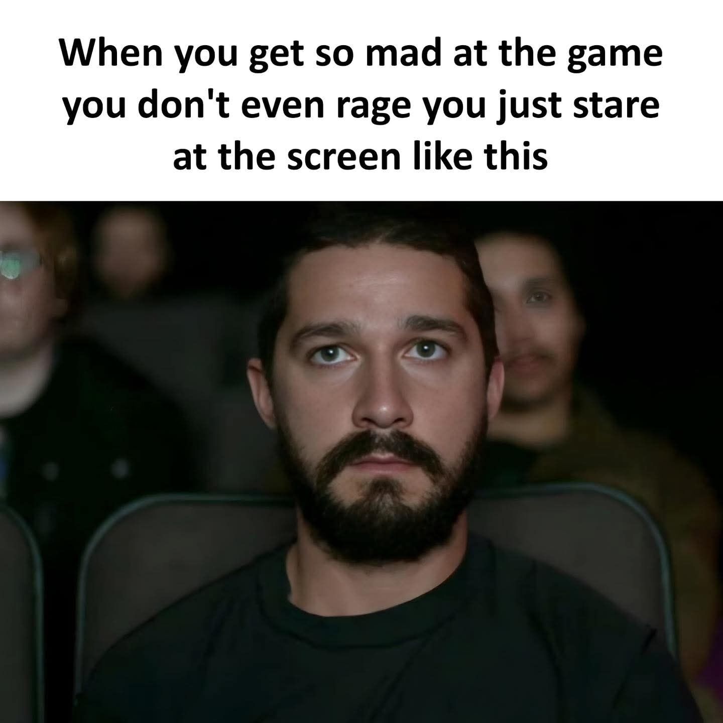 This single-panel reaction meme features bold black text on a white background at the top, followed by a candid photograph of actor Shia LaBeouf sitting in a dark movie theater. Shia has a completely blank, stoic, deadpan expression as he stares straight ahead, with no visible outward emotion. The top text reads 'When you get so mad at the game you don't even rage you just stare at the screen like this', referencing the relatable experience of being so frustrated by a poor performance or loss in a video game that you move past outward anger into quiet, suppressed, blank shock. The meme uses the actor's famously expressionless candid photo to perfectly illustrate this common relatable gaming scenario.