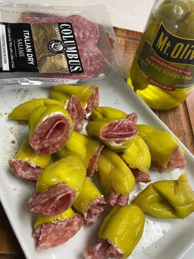 This meme showcases a quirky, visually clever food hack: slices of **Columbus Italian Dry Salami** wrapped inside **Mt. Olive Pepperoncini**, arranged on a white plate to closely resemble tortellini pasta. The image plays on the visual similarity between the folded pepperoncini-salami and traditional stuffed tortellini, presenting an unexpected, humorous food idea. The original ingredient packaging (salami bag and pepperoncini jar) is visible in the background, confirming the components used for this makeshift "pasta" creation.