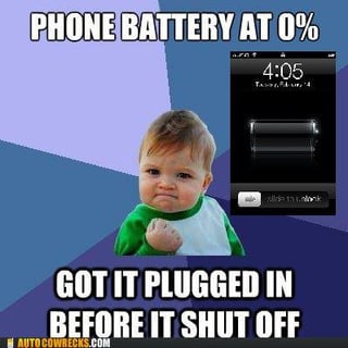 A meme featuring a baby with a smug expression and clenched fist, positioned to the left. To the right is an image of a smartphone screen displaying '4:05' and a battery icon at 0%. The text overlay reads 'PHONE BATTERY AT 0% GOT IT PLUGGED IN BEFORE IT SHUT OFF' in bold, uppercase letters. The background is a gradient of purple and blue, and the watermark 'AUTOCOMPLETES.COM' is visible at the bottom. The baby's expression and posture convey a sense of triumph or relief at successfully plugging in the phone before it died.