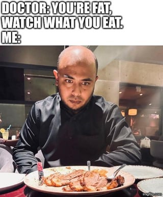 The meme has text at the top that reads: 'DOCTOR: YOU'RE FAT, WATCH WHAT YOU EAT. ME:'. Below the text is a photograph of a bald man wearing a black shirt, sitting at a restaurant table, staring intensely directly ahead at a large plate of cooked meat placed in front of him. The humor comes from intentional misinterpretation of the common phrase 'watch what you eat': the phrase normally means to monitor and limit your food consumption for health reasons, but the person in the meme interprets it literally as staring at (watching) the food he is eating.