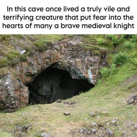 This is a single-panel anti-humor meme. The image displays a photograph of a small rocky cave opening in a grassy, rocky hillside. Text at the top sets up a spooky premise that the cave once housed an extremely vile, terrifying creature that frightened even the bravest medieval knights. The punchline comes from the original title of the post, which reveals the supposed terrifying creature is just an ordinary bunny, creating a silly anti-climax that subverts the audience's expectation of a dangerous monster.