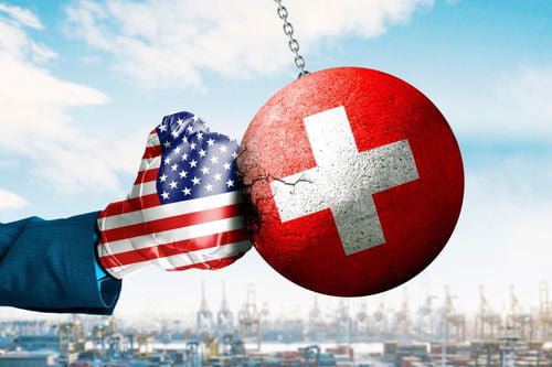 This is an illustrative meme visualizing the ongoing trade and military equipment dispute between the United States and Switzerland. The image shows an arm wearing a boxing glove printed with the flag of the United States punching a large cracked wrecking ball that is printed with the flag of Switzerland, against a blurred industrial port background. The visual metaphor represents the aggressive action the US took against Switzerland over the order dispute.