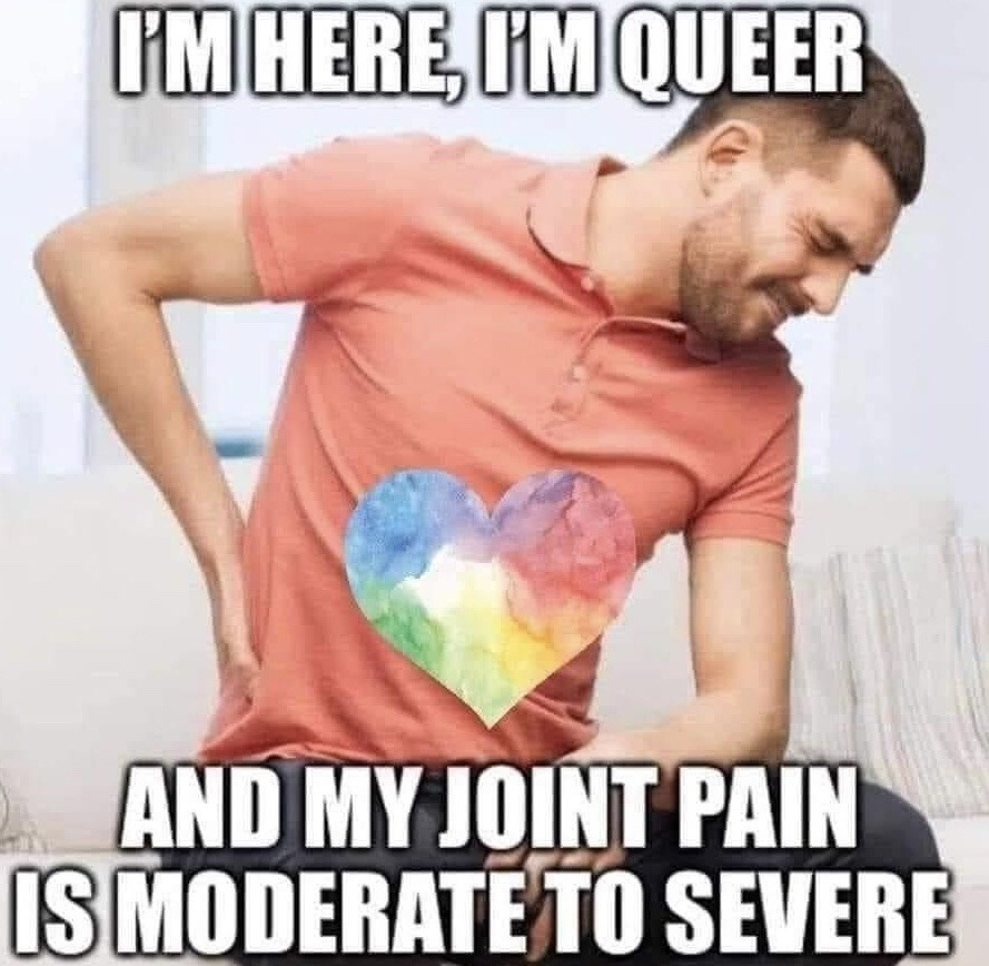This meme features a real man wearing a coral pink polo shirt with a watercolor-style rainbow pride heart printed on the front. He is hunched over, holding his lower back with a pained, grimacing expression, clearly experiencing physical discomfort. The text overlay parodies the common LGBTQ+ pride slogan: top text reads "I'M HERE, I'M QUEER", while the bottom text continues "AND MY JOINT PAIN IS MODERATE TO SEVERE". The joke is a relatable, self-deprecating combination of queer identity and common experiences of chronic or occasional joint/back pain, subverting the expected pride messaging for humorous effect.