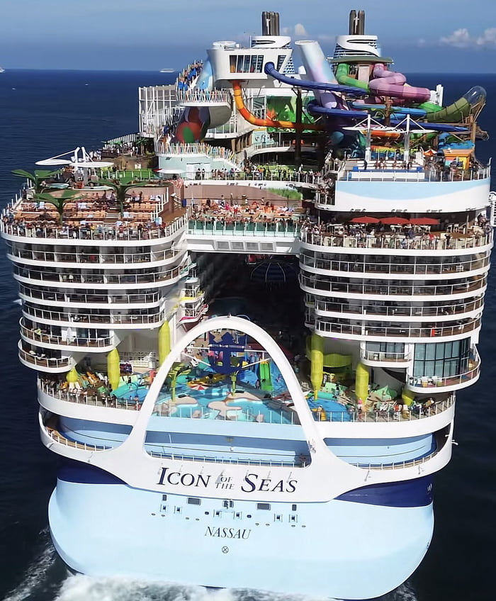 This image displays a frontal aerial view of the Icon of the Seas, the world's largest operating cruise ship registered in Nassau, sailing on open blue ocean. The massive vessel has dozens of multi-level decks packed with thousands of passengers, and visible on-board amenities include multiple colorful water slides, swimming pools, open-air dining areas, and public lounge spaces. The paired post title poses a sarcastic rhetorical question mocking the counterintuitive nature of transporting thousands of people on a giant ship across deep open sea, referencing widespread public concerns over cruise ship safety, hygiene, and risk of maritime incidents such as the Titanic disaster or other well-documented modern cruise mishaps. The joke highlights the perceived absurdity of large-scale cruise travel even as it remains a popular mainstream leisure option.