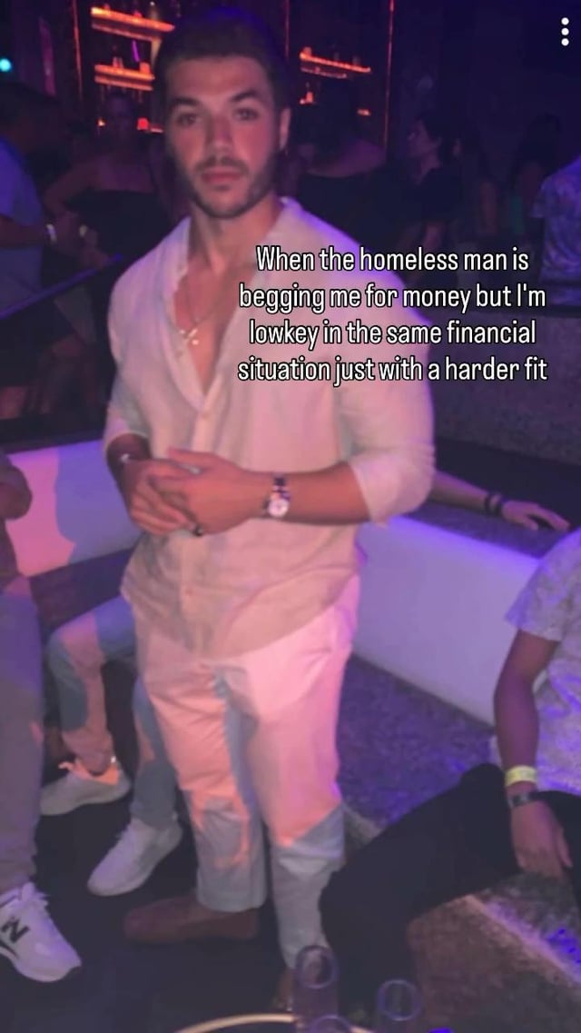 The meme is set in a dimly lit nightclub with purple ambient lighting, featuring a young man with facial hair standing at the center. He wears a stylish light unbuttoned button-down shirt, matching light trousers, a watch, and necklaces, and has a neutral, slightly blank expression as he looks at the camera. Overlaid text on the right side reads: 'When the homeless man is begging me for money but I'm lowkey in the same financial situation just with a harder fit'. The joke relies on relatable dark humor about being financially struggling (effectively as poor as an unhoused person asking for change) but dressing in nice, fashionable clothes that make others assume you have disposable income, leading to awkward, ironic situations. 'Harder fit' is internet slang for a more stylish, impressive outfit.
