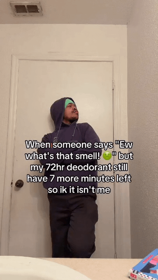 This is a relatable, humorous meme featuring a real person (a man in a dark hoodie with a green headband) leaning against a white interior door in a defensive, indignant posture. The on-image text reads: 
> When someone says 'Ew what's that smell! 🤢' but my 72hr deodorant still have 7 more minutes left so ik it isn't me

The joke centers on the absurd denial of being the source of a bad smell, clinging to the exact advertised duration of a deodorant product—even when it's only minutes from expiring. It leans into a funny, relatable everyday moment of refusing to accept responsibility for an unpleasant odor.