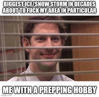 A meme featuring a real person with an amused and confident expression, standing in front of window blinds. The top text sets up the scenario: 'BIGGEST ICE/SNOW STORM IN DECADES ABOUT TO FUCK MY AREA IN PARTICULAR', while the bottom text humorously contrasts this impending crisis with the character's preparedness: 'ME WITH A PREPPING HOBBY'. The character's smile and relaxed demeanor emphasize the joke about being ready for the storm due to their prepping hobby.