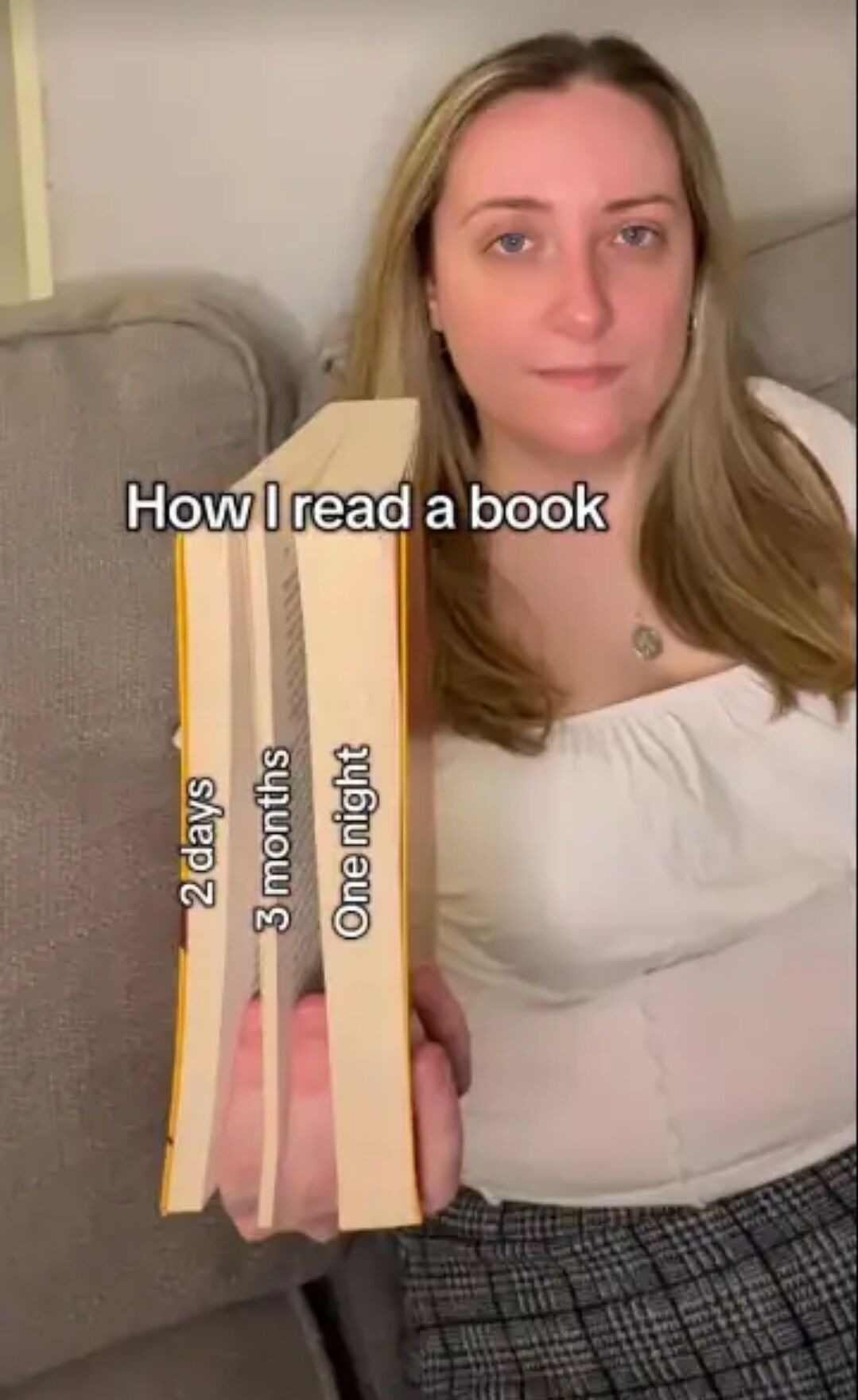 This relatable meme features a real woman sitting on a couch holding three fanned-out book segments that joke about a common uneven reading habit. The top overlay text reads 'How I read a book', with each segment labeled by how long it took the reader to finish that portion: the thin starting segment is labeled '2 days', the even thinner middle section is labeled '3 months', and the thick final section of the book is labeled 'One night'. This illustrates how many readers drag out the start and middle of a book for months, then binge the entire ending in a single sitting once they get fully invested or close to a deadline.