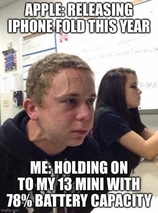 This meme uses the popular stressed, sweating male student reaction template. The top text states that Apple is releasing an iPhone Fold model in the current year, while the bottom text reads 'Me: Holding on to my 13 Mini with 78% battery capacity'. The strained, anxious expression of the man in the image conveys the user's frustration and dedication to holding onto their small form factor iPhone 13 Mini rather than upgrading to the new foldable device Apple is launching, expressing a widespread desire among consumers for Apple to release a new iPhone Mini model instead of focusing solely on larger or foldable devices.