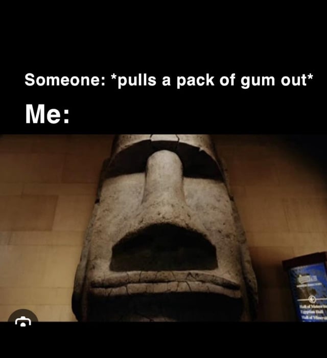 The meme consists of two sections: top text and a lower image. The top text reads: 'Someone: *pulls a pack of gum out* Me:' which sets up a relatable scenario. Below the text is a photograph of a large, solemn stone Moai statue face (characteristic of Easter Island) displayed in a museum, with a tiled wall background and a small informational sign visible to the right. The humor arises from the contrast between the casual action of pulling out gum and the Moai's intense, serious expression, implying an exaggeratedly dramatic reaction to the situation.