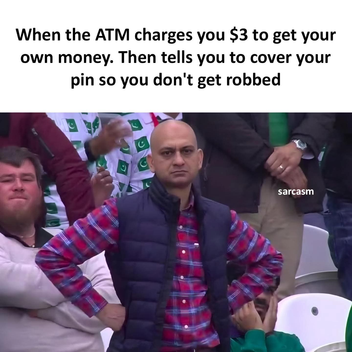 This is a single-panel reaction meme. The top of the image contains text that reads: 'When the ATM charges you $3 to get your own money. Then tells you to cover your pin so you don't get robbed'. The visual paired with the text is a widely recognized viral photo of a bald Pakistani man at a sports match, standing with his hands on his hips, wearing a red plaid shirt under a dark puffer vest, with a deadpan, unimpressed, annoyed expression. The image perfectly conveys the sarcastic frustration of the joke: pointing out the irony that banks charge customers unfair fees to access their own money (essentially robbing them), while simultaneously advising customers to protect their PIN to avoid being robbed by others. A small watermark reading 'sarcasm' is present on the right side of the visual section, over the background crowd.