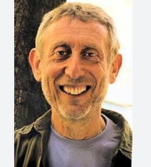 This is an outdoor portrait photograph of Michael Rosen, the famous British children's author and widely recognized internet meme icon. He is facing the camera directly with a wide, joyful toothy smile. He has short grey hair, light grey stubble and wrinkles, wears a light purple t-shirt under a dark unbuttoned collared jacket, and stands next to a dark tree trunk with a bright blurred background behind him. The image is shared as a birthday tribute to honor his 80th birthday, acknowledging his status as a beloved "meme lord" for his widely circulated expressive reaction images across social media.
