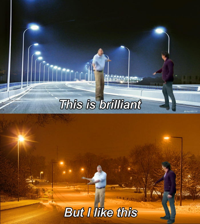 A two-panel comparison meme contrasting modern and nostalgic street lighting. The top panel depicts a nighttime bridge illuminated by bright white LED streetlights, with two men (one in a light blue shirt and the other in a purple jacket) gesturing animatedly; overlaid text reads 'This is brilliant'. The bottom panel shows a snowy nighttime street lit by warm orange sodium vapor streetlights, featuring the same two men in similar gesturing poses; overlaid text reads 'But I like this'. The meme evokes nostalgia by juxtaposing the perceived 'brilliance' of modern white lights with the preferred warmth of classic sodium lights.