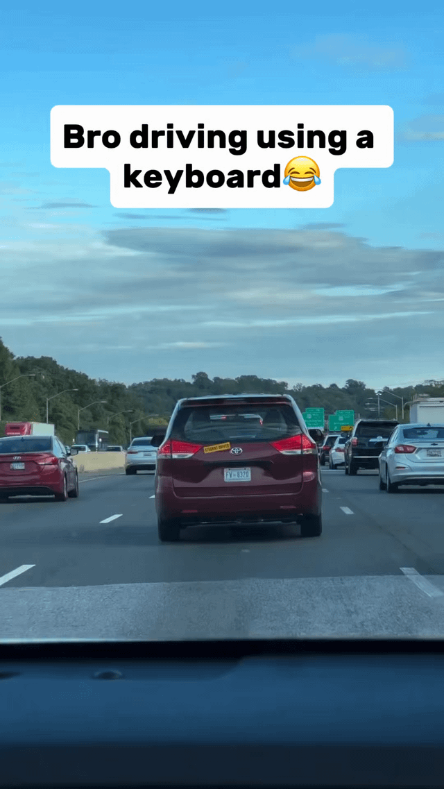 This is a first-person candid photo taken from inside a moving vehicle on a multi-lane highway during daytime. In the center of the frame, a maroon Toyota minivan drives ahead, with a small yellow rectangular sticker on its rear window that visually matches the WASD key set from a standard PC gaming keyboard. A white text overlay at the top of the image reads "Bro driving using a keyboard 😂", making a humorous joke comparing operating a real car to controlling a character in a PC video game with WASD movement keys, implying the driver uses the sticker "keys" to drive the van. Other vehicles fill adjacent highway lanes, with tree lines, green highway directional signs, and a partly cloudy bright blue sky visible in the background. The bottom edge of the frame shows the dashboard of the car the photo was captured from.