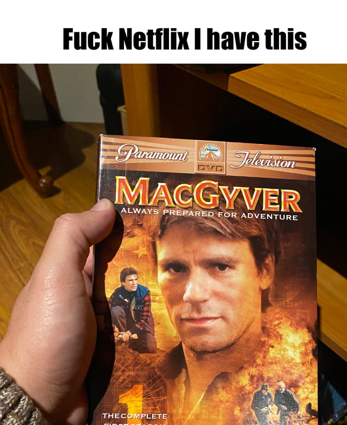A photograph showing a hand holding a Paramount Television DVD case for 'MacGyver: The Complete First Season' with the text 'Fuck Netflix I have this' overlaid at the top. The DVD cover features the main character MacGyver with a serious expression, surrounded by action imagery including fire and other characters in adventurous poses. The tagline 'ALWAYS PREPARED FOR ADVENTURE' is visible on the cover.