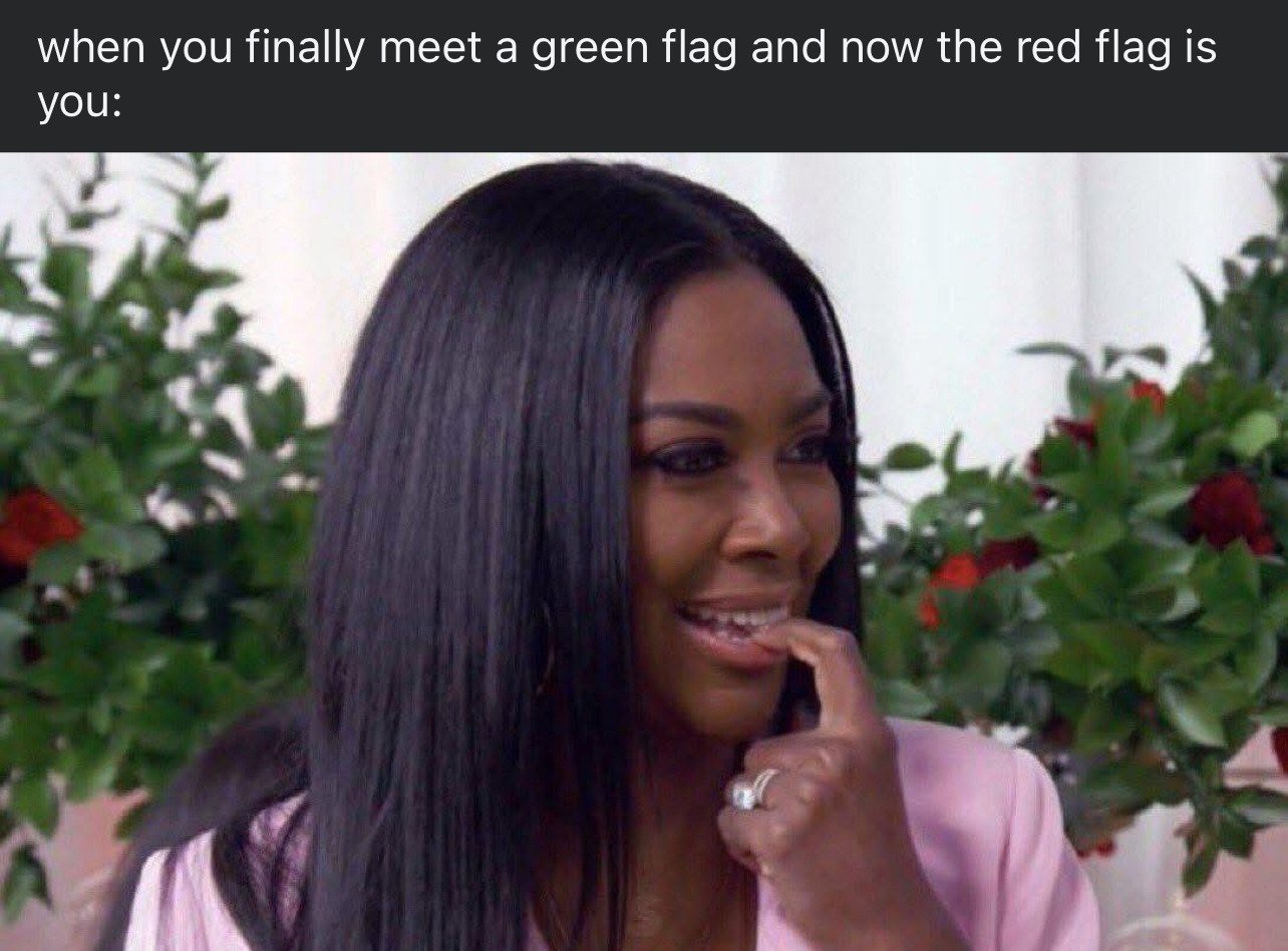 The meme consists of two parts: a text header at the top that reads 'when you finally meet a green flag and now the red flag is you:', followed by a reaction photo of reality TV star Kenya Moore. She has an awkward, guilty, nervous expression, is smiling faintly while biting her index finger, and looking off to the side as if she has been caught being in the wrong. 'Green flag' is internet slang for a romantic partner who has healthy, positive, desirable traits, while 'red flag' refers to toxic, problematic, undesirable traits in a person. The joke is self-deprecating relatable humor about people who have their own unhealthy relationship patterns realizing they are the problematic party when they meet a genuinely good partner.