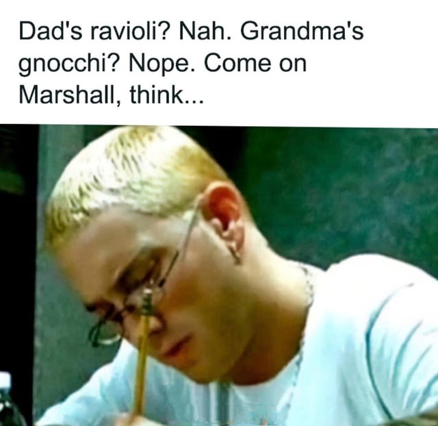 This is a single-panel humorous meme featuring a candid photo of rapper Eminem (real name Marshall Mathers) wearing thin-rimmed glasses and a white t-shirt, looking down with a concentrated, thoughtful expression as if he is trying hard to recall something. The overlaid text at the top reads: 'Dad's ravioli? Nah. Grandma's gnocchi? Nope. Come on Marshall, think...' The joke is a direct reference to the famous line about 'mom's spaghetti' from Eminem's iconic 2002 song Lose Yourself, which is a widely referenced meme lyric. The meme teases Marshall to remember the well-known pasta associated with his music, rather than the other Italian pasta dishes made by other family members listed.