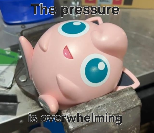 This meme features a real plastic Jigglypuff figurine from the Pokemon franchise clamped tightly inside a metal bench vise, appearing squished and strained. Text overlaid at the top reads 'The pressure' and at the bottom reads 'is overwhelming', creating a relatable joke about feeling overburdened by stress, work, or life pressures that feel impossible to manage.