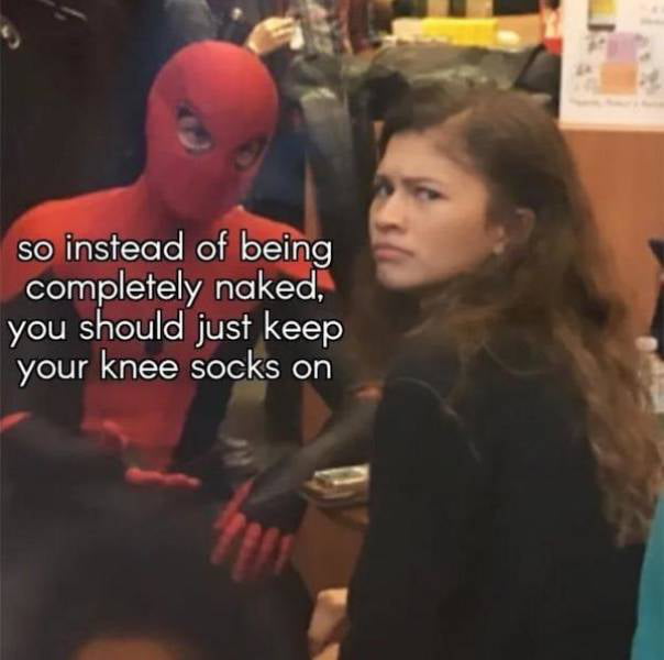 An image featuring two individuals: one dressed in a red and black Spider-Man costume (left) and another with long brown hair wearing a black top (right). The Spider-Man-costumed individual gestures with their hands, while the other person looks to the side with a neutral expression. Overlaid white text on the left reads: 'so instead of being completely naked, you should just keep your knee socks on', creating a humorous, suggestive joke.