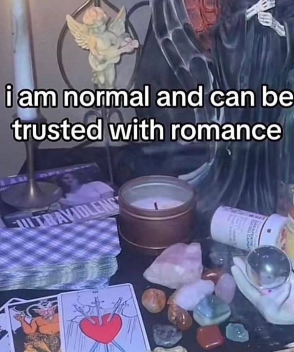 The meme displays a personal spiritual altar filled with items tied to witchcraft, alternative culture, and romantic angst: a copy of Lana Del Rey's Ultraviolence album, the Three of Swords tarot card (a symbol of heartbreak, grief, and romantic trauma), a stack of tarot cards, multiple rough and tumbled healing crystals, a tin candle, a small cherub figurine, a dark robed skeleton figurine, and a tall white candle. Bold overlaid text reads "i am normal and can be trusted with romance", creating a sarcastic humorous contrast between the claim of being emotionally stable for romantic relationships and the obvious visual evidence of items tied to intense, often messy or painful romantic experiences and niche spiritual interests that imply the poster is far from conventional when it comes to love.
