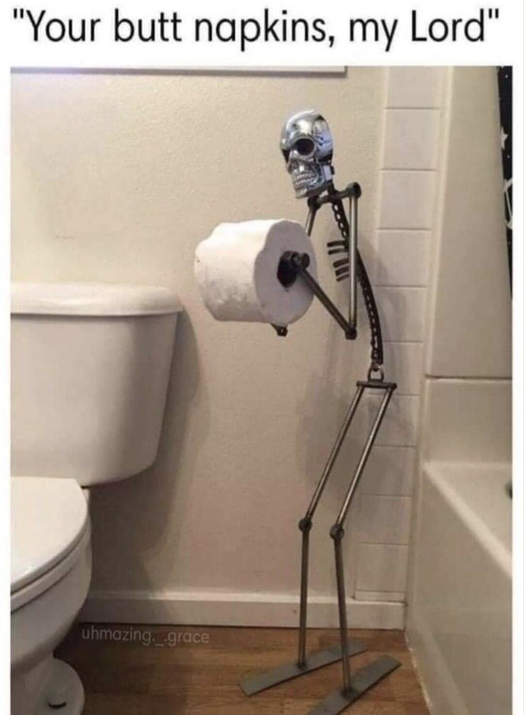 The image shows a quirky novelty bathroom decor item positioned next to a standard white toilet: a standing metal skeleton figurine designed to work as a toilet paper holder, posed like a polite bowing butler holding out a roll of toilet paper. A funny caption at the top reads "Your butt napkins, my Lord", which jokes about framing toilet paper as fancy formal napkins being served by the skeleton servant, leaning into the absurd juxtaposition of a high-end butler service dynamic with the mundane, silly context of bathroom supplies. A watermark for the original photographer uhmazing._.grace appears at the bottom left of the photo.