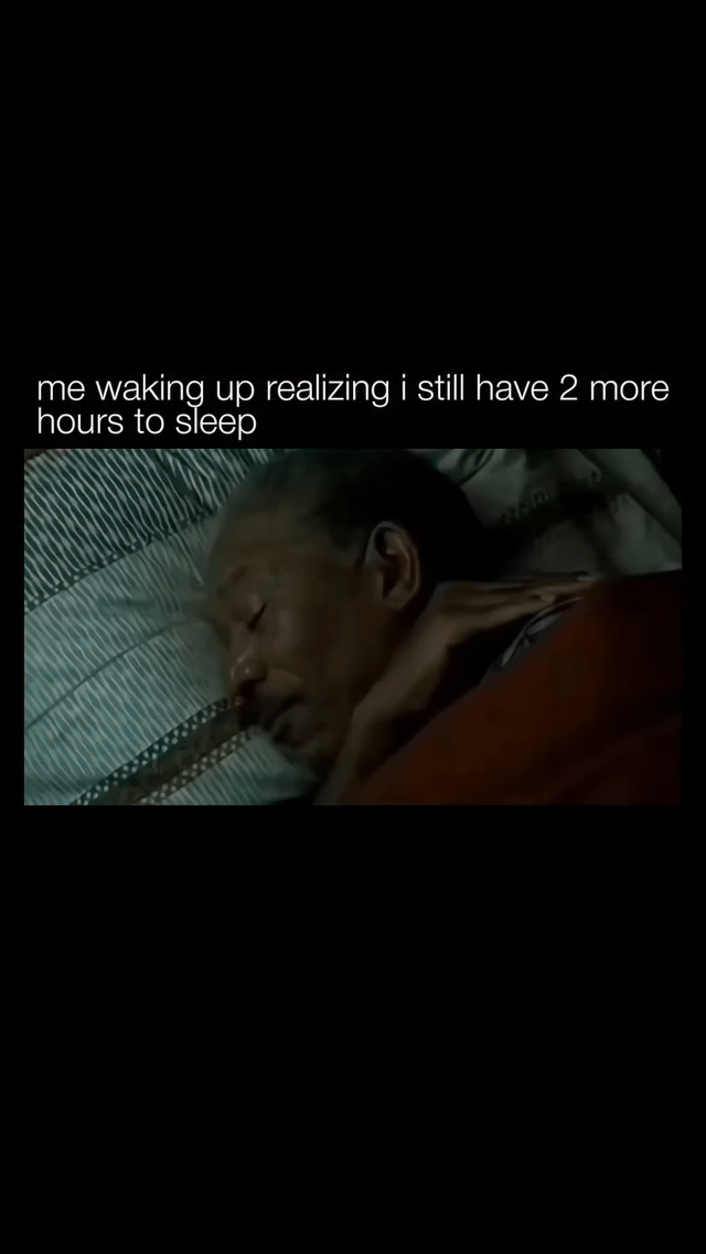 This meme uses a black background with white top text that reads 'me waking up realizing i still have 2 more hours to sleep', paired with a film still of actor Morgan Freeman lying in bed, eyes closed, looking extremely relaxed and content as he prepares to go back to sleep. It humorously captures the widely relatable, very positive feeling of waking up earlier than required and realizing you have extra time left to rest before you need to get up.
