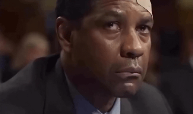 A close-up image of a man with a bandage on his forehead, dressed in a dark suit and light blue shirt. He appears to be in a formal setting, possibly a meeting or public event, with a serious and contemplative expression. The background is blurred, focusing attention on his face and upper body.