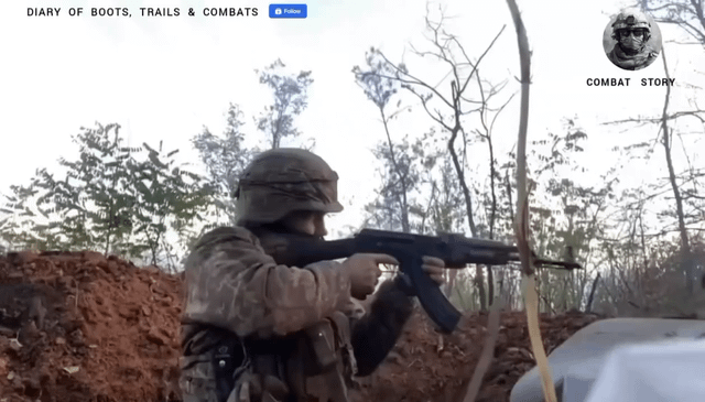 The image depicts a soldier in military gear, including a helmet and uniform, crouched in a dirt embankment while aiming a rifle. The background features leafless trees, suggesting a wooded or rural environment. At the top left, the text 'DIARY OF BOOTS, TRAILS & COMBATS' is displayed, with a small blue button next to it. On the top right, there is a circular icon containing a person's face, accompanied by the text 'COMBAT STORY'.