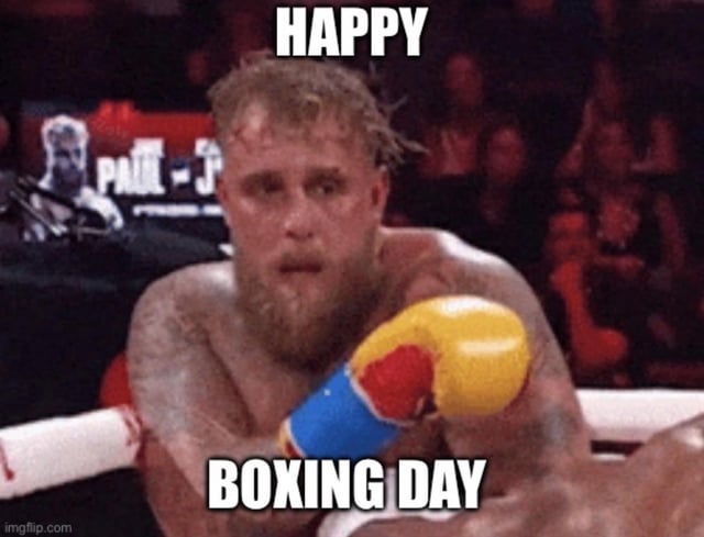 A meme featuring a real male boxer with visible tattoos, wearing yellow and red boxing gloves, sitting in a boxing ring. The image has bold white text at the top reading 'HAPPY' and at the bottom reading 'BOXING DAY', creating a pun on the holiday Boxing Day by visually associating it with the sport of boxing. The background shows a blurred audience, and there is a watermark 'imgflip.com' in the bottom left corner.