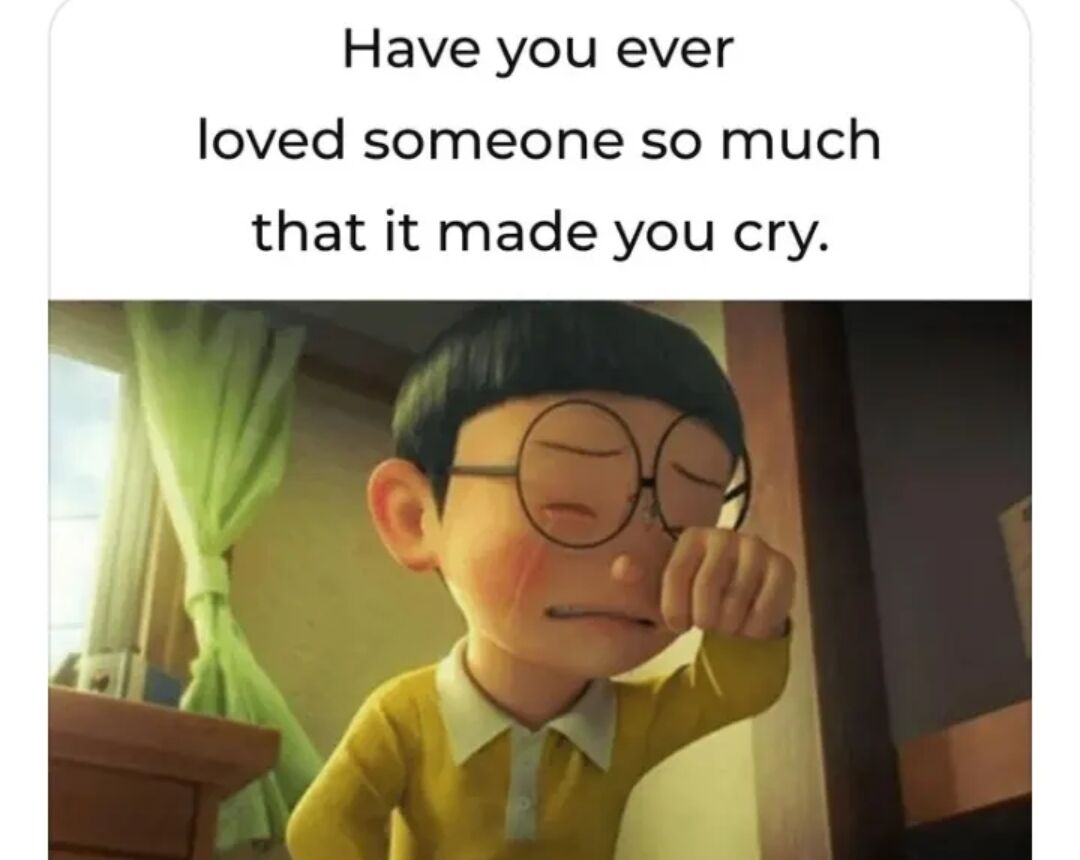 The image features a top section with text reading 'Have you ever loved someone so much that it made you cry.' Below the text is a screenshot of an animated character: a young person with short black hair, round glasses, wearing a yellow shirt with a white collar. The character has closed eyes, blushing cheeks, and is wiping their eye with their right hand, conveying a tearful, emotional state. The background shows a room with green curtains and sunlight streaming through a window, creating a warm, intimate atmosphere. The combination of the text and the character's expression emphasizes deep, heartfelt love that evokes tears.