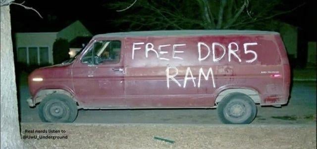 A nighttime photograph of a worn red van parked on a residential street. The side of the van features handwritten white text reading 'FREE DDR5 RAM,' a satirical reference to the 'free candy' van trope but targeted at tech enthusiasts. The bottom of the image contains a watermark: 'Real nerds listen to @level_underground.' The van appears to have a driver, though their features are indistinct due to the low lighting. The scene humorously subverts the classic 'suspicious van' stereotype by replacing 'candy' with high-demand computer memory (DDR5 RAM), appealing to the tech community's obsession with hardware upgrades.