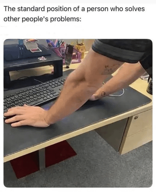 The meme consists of a top text caption followed by a candid office photograph. The top text reads 'The standard position of a person who solves other people's problems:'. The photograph shows a person (only their arms and part of their torso are visible) leaning far over an office desk: one hand rests on a keyboard on the desk, while their other arm is propped under their opposite armpit, as they hover over the workspace typically occupied by another person. The joke is a relatable reference to the extremely common real-world behavior of tech support staff, IT workers, or tech-savvy coworkers/friends leaning over someone else's desk to troubleshoot their computer or device issue, rather than sitting down in the user's seat to fix the problem.