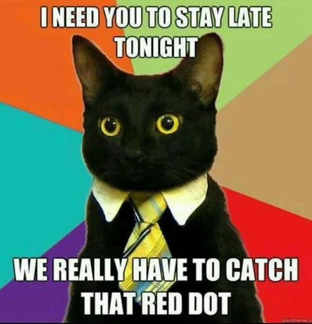 A meme image featuring a black cat with striking yellow eyes, dressed in a white collared shirt and yellow striped tie, set against a bold, multicolored background of orange, green, blue, red, and purple. The cat exhibits an intense, authoritative expression, mimicking a strict boss. Overlaid text reads: 'I NEED YOU TO STAY LATE TONIGHT' (top) and 'WE REALLY HAVE TO CATCH THAT RED DOT' (bottom). The humor stems from anthropomorphizing the cat as a demanding boss, with the absurdly trivial 'urgent task' of catching a laser pointer red dot, a classic feline obsession.