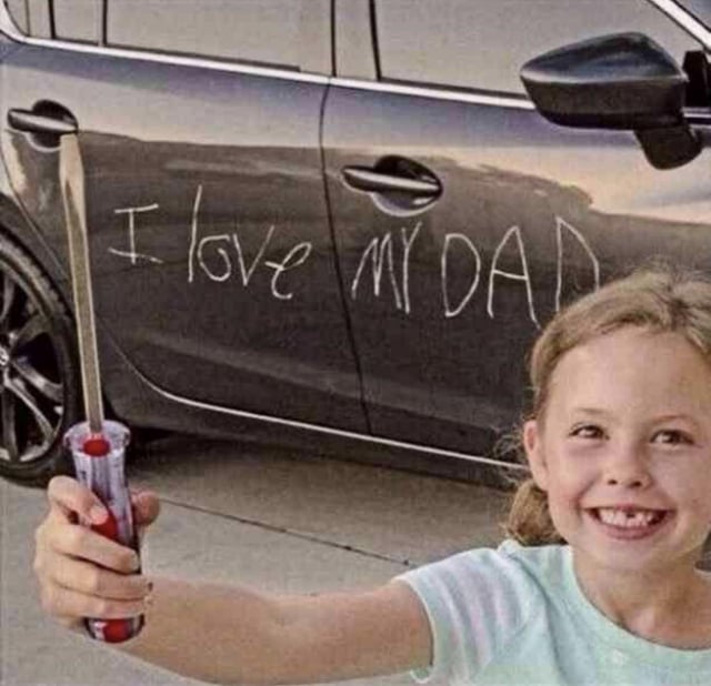 A photograph featuring a young girl with blonde hair, wearing a light blue shirt, smiling brightly while holding a red and clear screwdriver in her right hand. Behind her is a dark-colored car, and on the car's front door, there is handwritten white text that reads 'I love my DAD'. The girl stands in front of the car, appearing proud and happy, with the screwdriver humorously positioned as if she used it to write the message (though the text is likely in washable marker or chalk to avoid damaging the car).