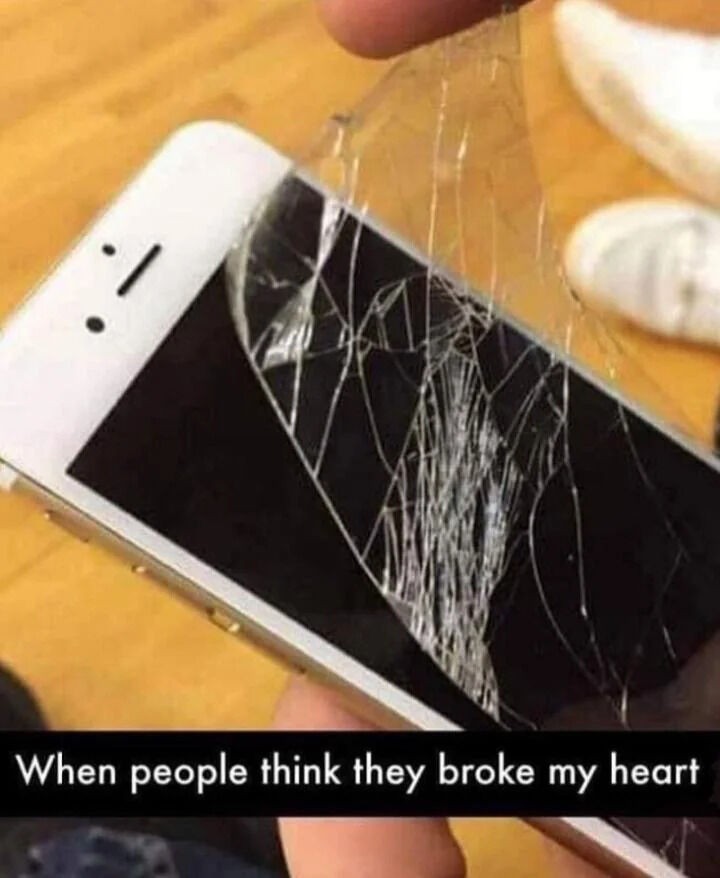 This meme shows a close-up of a person holding an older model white iPhone, peeling a heavily cracked tempered glass screen protector off the fully undamaged phone screen underneath. The text at the bottom reads 'When people think they broke my heart', using the visual as a humorous metaphor: the cracked outer screen protector stands for a superficial, seemingly hurt outer facade, while the unbroken phone screen underneath represents the poster's actual unharmed core feelings. The joke plays on the relatable scenario where others assume they have emotionally hurt someone, when only that person's minor, superficial feelings were impacted, leaving their true emotional state completely fine.