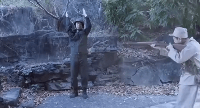 The meme image depicts two individuals in an outdoor, rocky area with trees in the background. One person, dressed in dark clothing and a helmet, stands with arms raised above their head, palms facing forward, in a surrendering posture. The other individual, wearing light-colored clothing and a cap, holds a rifle pointed at the surrendering person. The title 'Never surrender lol' creates an ironic contrast between the action of surrender and the text, infusing humor into the scene.
