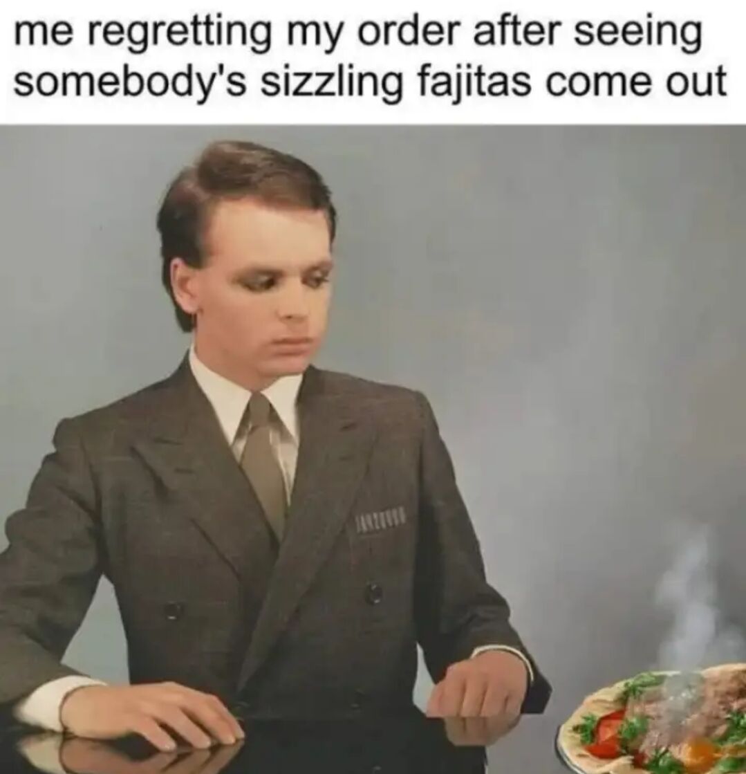 This is a relatable meme that captures the common experience of food envy when dining out at a restaurant. The top text reads 'me regretting my order after seeing somebody's sizzling fajitas come out'. Below the text, a man in a suit sits at a table with a downcast, regretful expression, looking towards a hot, steaming plate of sizzling fajitas next to him, clearly wishing he had ordered the fajitas instead of his own meal. The meme perfectly illustrates the universal feeling of second-guessing your food order when you see a more appealing dish served to another diner.