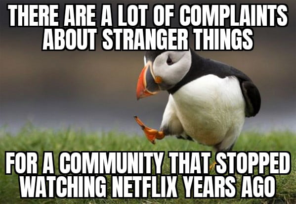 A meme featuring a photograph of a puffin bird standing on green grass with one foot lifted. The top text reads 'THERE ARE A LOT OF COMPLAINTS ABOUT STRANGER THINGS' and the bottom text reads 'FOR A COMMUNITY THAT STOPPED WATCHING NETFLIX YEARS AGO'. The humor lies in the sarcastic observation that a community which claims to have stopped using Netflix years ago still complains about the show 'Stranger Things' (a Netflix original series).