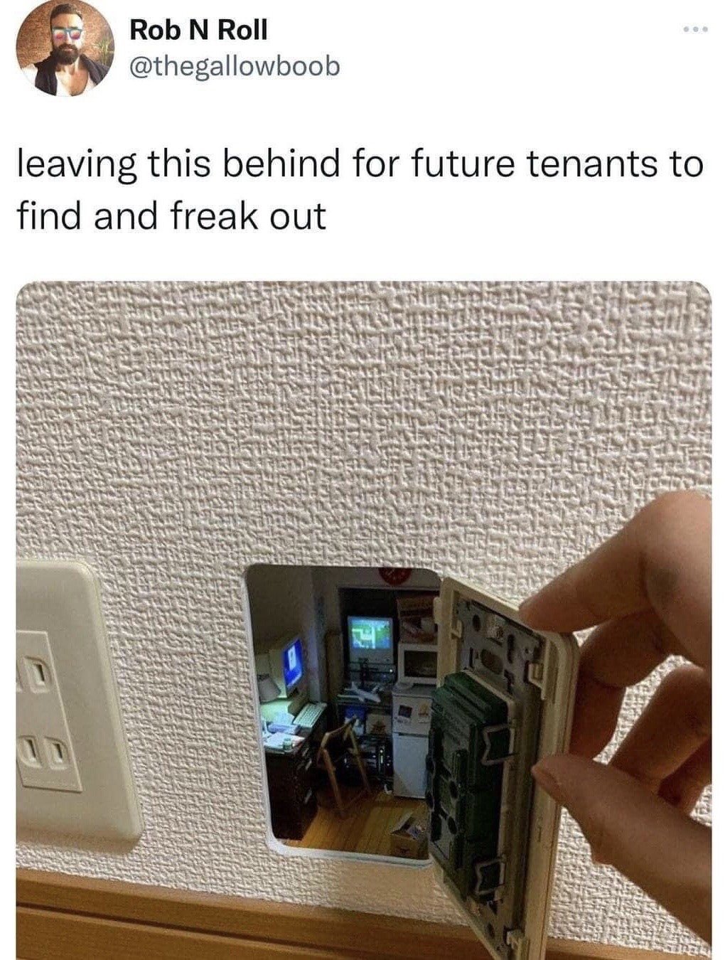 This is a screenshot of a viral X (formerly Twitter) post. The poster states they are leaving a prank for future tenants to discover. The attached photo shows a hand pulling open a standard residential wall light switch cover, revealing a tiny, highly detailed miniature diorama of a late 90s/early 2000s home office built into the wall cavity behind the switch. The diorama includes small CRT desktop computers, a desk, chair, and other small furniture, making it look like a tiny hidden room exists inside the wall, designed to confuse and startle anyone who opens the switch cover for maintenance.