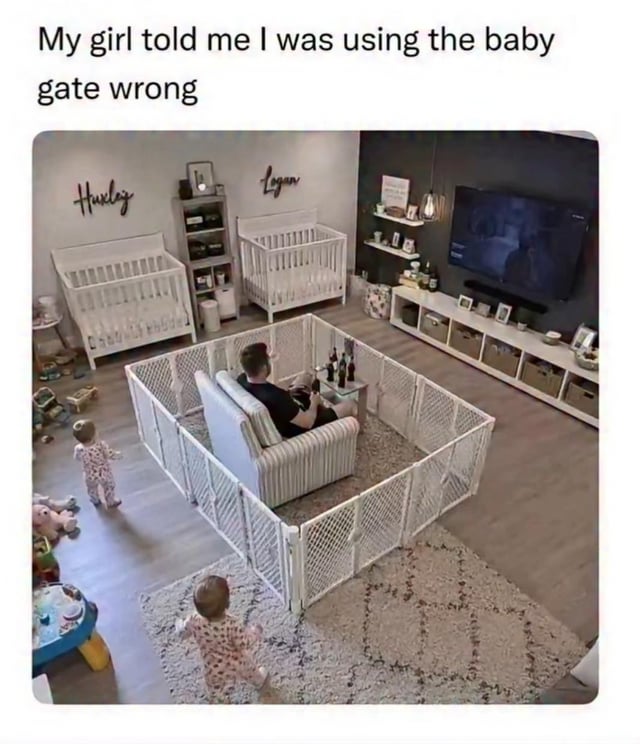 The meme features top text that reads "My girl told me I was using the baby gate wrong", above a photograph of a home living space with two baby cribs, with the names "Huxley" and "Logan" mounted as wall decor above each crib. In the center of the room, a man is seated comfortably on an armchair inside a large enclosed baby safety gate, with a small table next to him holding multiple bottles of beer, facing a turned-on TV. Two toddler children are standing outside the baby gate, looking in at the man. The humor comes from the subversion of the intended use of a baby gate: instead of containing the children inside the gate to keep them safe, the man used the gate to fence himself into a private, undisturbed space to relax, drink, and watch TV without interruptions from his kids.