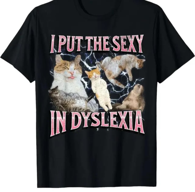 A black t-shirt featuring bold pink text that reads 'I PUT THE SEXY IN DYSLEXIA' in two lines. Between the text, there are several cats in various playful and relaxed poses: one with its tongue out, a kitten, and others lying or stretching. The background includes a subtle lightning effect, enhancing the dynamic look. The design uses wordplay, humorously inserting 'sexy' into 'dyslexia' for comedic effect, paired with cute cat imagery to boost appeal.
