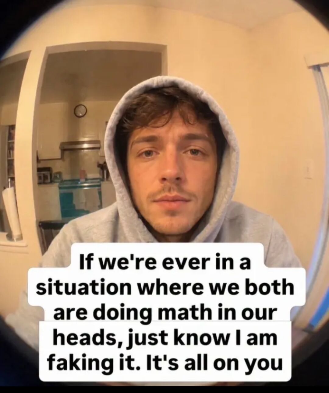 This is a relatable single image meme featuring a fisheye lens selfie of a young man in a light grey hoodie, looking straight at the camera with a neutral, earnest expression. The background shows a typical home interior with a kitchen area visible through a doorway. Overlaid on the bottom of the image is text that jokes that if the viewer and the poster are ever in a situation where they both need to do mental math, the poster is faking their calculations and all the math work is up to the viewer. The meme resonates with people who struggle with mental arithmetic, such as when splitting bills, calculating totals, or solving quick math problems in social situations.