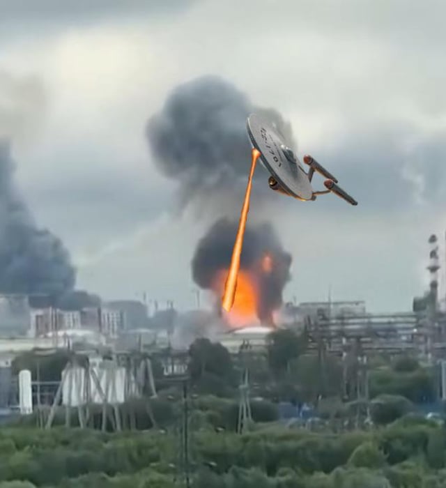 This edited composite meme image features the USS Enterprise NCC-1701 starship from the Star Trek franchise flying over an urban/industrial area under an overcast sky. The Enterprise is shown firing a bright orange energy beam directly at the ground, which has caused a large explosion with multiple plumes of thick dark smoke rising from the impact site. The joke of the meme references Star Trek's core Prime Directive rule, which prohibits Starfleet personnel from interfering with the internal development of less advanced civilizations; the ship openly attacking a populated area is a direct, extreme violation of this rule, which aligns with the given title.