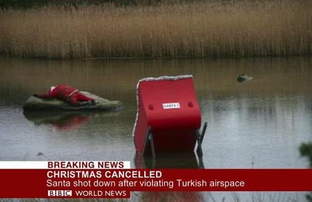 A satirical fake BBC World News breaking news screenshot. The headline in bold red text reads 'BREAKING NEWS CHRISTMAS CANCELLED' with a subheadline 'Santa shot down after violating Turkish airspace'. The visual shows a person dressed in a Santa Claus costume lying motionless on a rock partially submerged in water. To the right, a red object labeled 'SANTA' is tilted and half-submerged. The background features tall, dry grass along the water's edge, creating a somber yet absurd scene. The BBC World News logo is displayed at the bottom left, mimicking a genuine news broadcast.