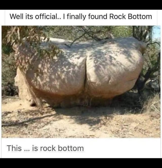 A humorous meme featuring a photograph of a large, naturally occurring rock formation that visually resembles two rounded, buttock-like shapes. The rock is positioned in a dry, outdoor setting with sparse vegetation and tree branches partially surrounding it. Overlaid text at the top of the image reads 'Well its official.. I finally found Rock Bottom' and additional text at the bottom states 'This ... is rock bottom,' creating a pun on the common idiom 'rock bottom' (referring to the lowest point in life) by depicting it as a literal rock.