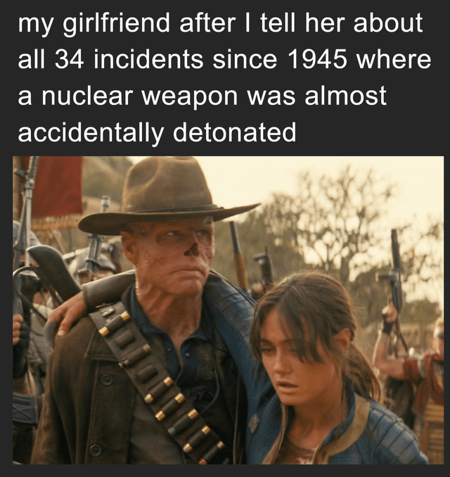 A meme combining a movie screenshot with a humorous text overlay. The text at the top reads: 'my girlfriend after I tell her about all 34 incidents since 1945 where a nuclear weapon was almost accidentally detonated'. The image depicts a weathered man in a cowboy hat with his arm around a visibly tired woman, standing among armed individuals in a dry, desolate landscape. The humor arises from the contrast between the intense, post-apocalyptic visual tone (suggesting exhaustion or trauma) and the relatable scenario of a partner being overwhelmed by excessive, heavy information dump about historical nuclear near-disasters.