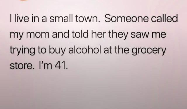 This is a text-only meme set against a soft pale pink gradient background. The joke follows a short anecdote: the narrator lives in a small town, where a local resident called the narrator's mother to report that they saw the narrator trying to buy alcohol at a grocery store. The punchline reveals the narrator is 41 years old, a fully legal adult, making the nosy overreach and unnecessary reporting by the town resident absurd and humorous, highlighting the lack of privacy and overly involved gossip culture common in small tight-knit communities.