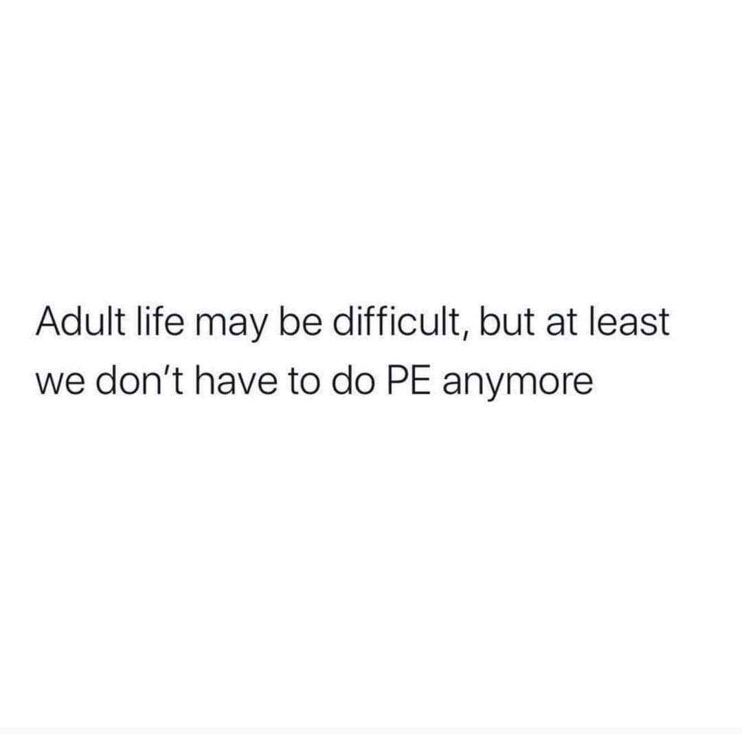 This is a minimalist text-only meme set against a plain solid white background. The black text reads: 'Adult life may be difficult, but at least we don't have to do PE anymore'. The meme highlights a small, relatable positive of adulthood by referencing the widespread shared experience of dreading mandatory physical education (PE) classes during primary and secondary school, offering a lighthearted, humorous silver lining to the stresses of being an adult.
