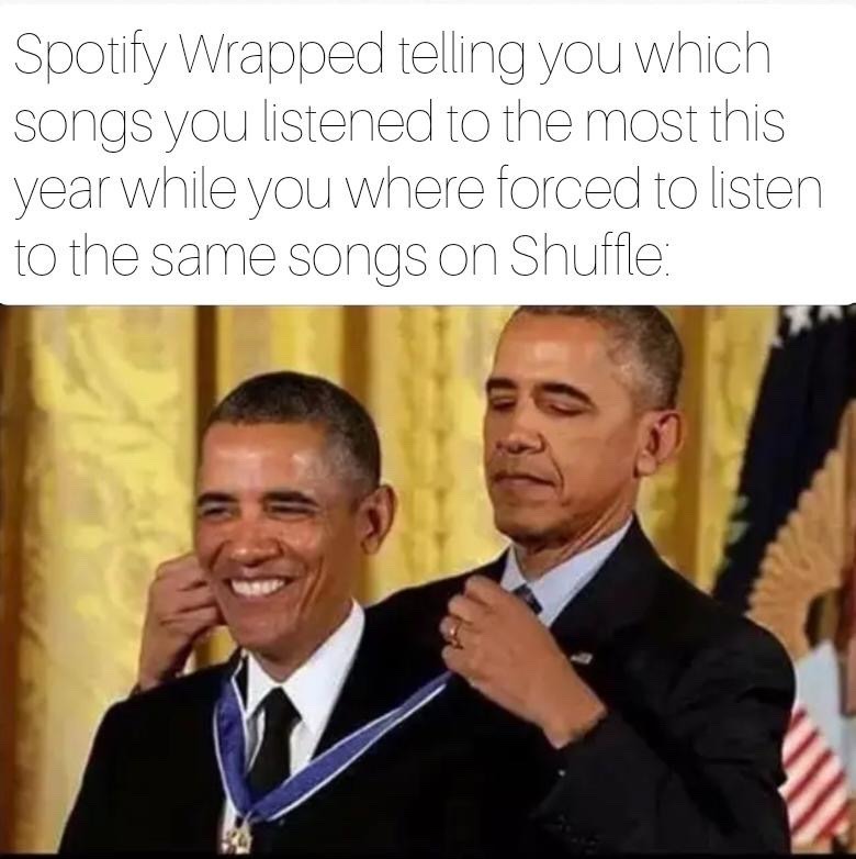 The meme has text at the top that reads 'Spotify Wrapped telling you which songs you listened to the most this year while you where forced to listen to the same songs on Shuffle:'. Below the text is an edited photo of former US president Barack Obama appearing to award a Presidential Medal of Freedom to a duplicate of himself. The version of Obama receiving the medal has a wide, happy grin, while the version presenting the medal has a calm, slightly smug expression. The meme jokes that Spotify Wrapped highlights your most played songs as if they are a deliberate personal choice, when in reality many users hear the same tracks repeatedly because Spotify's shuffle algorithm frequently cycles through the same small selection of songs from their library, making the year-end summary feel like an unearned, meaningless award for a habit the user did not intentionally choose.
