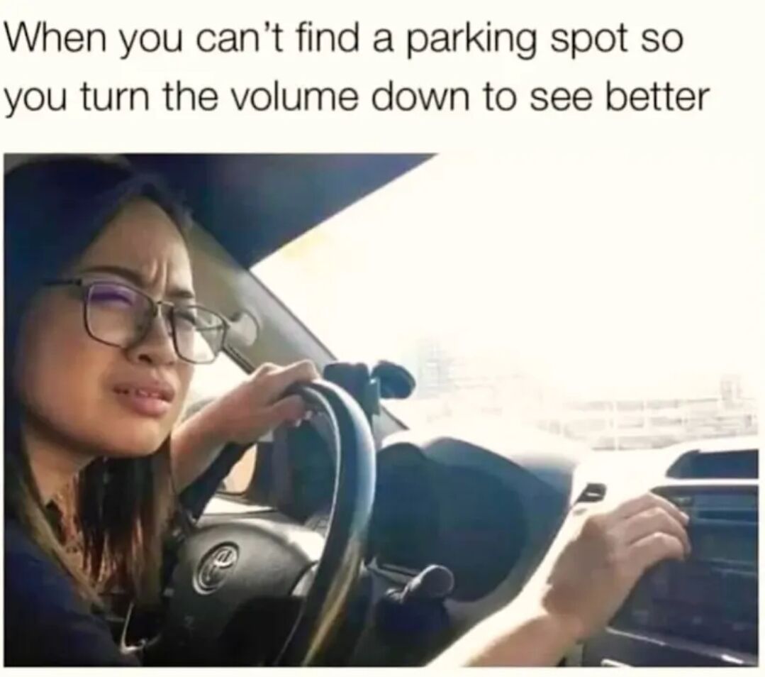 A meme featuring a photograph of a person driving a car. The individual is holding the steering wheel with their left hand and appears to be adjusting the volume control with their right hand. Above the image, there is text that reads: 'When you can't find a parking spot so you turn the volume down to see better.' The humor lies in the relatable, albeit illogical, action of reducing volume to improve visibility, playing on the common human tendency to use unrelated senses to focus.